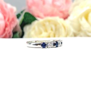 A sterling silver 5-stone band featuring alternating round lab blue sapphires and moissanites. The band has a classic design with the gemstones set in a row with three sapphires and two moissanites. Displayed on a white surface with a pastel floral background.