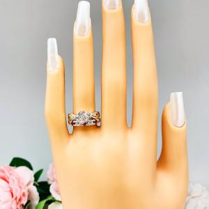 Mannequin hand with long white shimmery nails, displayed against a soft white-gray background with pink and white floral accents. The hand is wearing a sterling silver 5-stone band featuring alternating round lab rubies and moissanites. The band has a classic design with the gemstones set in a row with three rubies and two moissanites. Shown with a round moissanite solitaire ring with leaf design (not included).