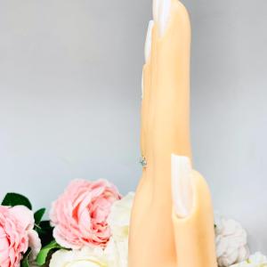 Mannequin hand with long white shimmery nails, displayed against a soft white-gray background with pink and white floral accents. The hand is wearing a sterling silver 5-stone band set with 3mm round sparkling aquamarine blue moissanites.