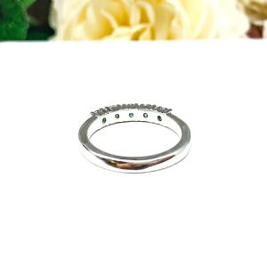 A sterling silver 5-stone band set with 3mm round sparkling aquamarine blue moissanites. Displayed on a white surface with a floral background.