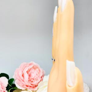 Mannequin hand with long white shimmery nails, displayed against a soft white-gray background with pink and white floral accents. The hand is wearing a sterling silver 5-stone band featuring alternating round lab blue sapphires and moissanites. The band has a classic design with the gemstones set in a row with three sapphires and two moissanites.