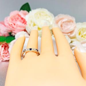 Mannequin hand with long white shimmery nails, displayed against a soft white-gray background with pink and white floral accents. The hand is wearing a sterling silver curved 5-stone band featuring alternating round lab blue sapphires and moissanites. The band has a classic design with the gemstones set in a row with three sapphires and two moissanites.