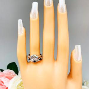 Mannequin hand with long white shimmery nails, displayed against a soft white-gray background with pink and white floral accents. The hand is wearing a sterling silver 5-stone band featuring alternating round lab blue sapphires and moissanites. The band has a classic design with the gemstones set in a row with three sapphires and two moissanites. It is featured here with an east/west oval-cut moissanite solitaire ring (not included).