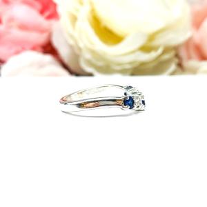 A sterling silver curved 5-stone band featuring alternating round lab blue sapphires and moissanites. The band has a classic design with the gemstones set in a row with three sapphires and two moissanites. Displayed on a white surface with a pastel floral background.