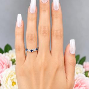 A woman's hand wearing a sterling silver curved 5-stone band featuring alternating round lab blue sapphires and moissanites. The band has a classic design with the gemstones set in a row with three sapphires and two moissanites. Model image for size and styling reference — not a photo of the actual ring.