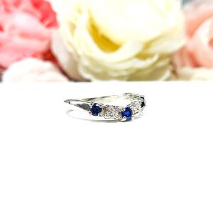A sterling silver curved 5-stone band featuring alternating round lab blue sapphires and moissanites. The band has a classic design with the gemstones set in a row with three sapphires and two moissanites. Displayed on a white surface with a pastel floral background.