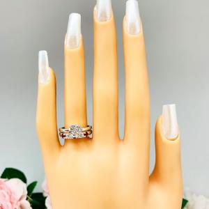 Mannequin hand with long white shimmery nails, displayed against a soft white-gray background with pink and white floral accents. The hand is wearing a sterling silver 5-stone band featuring alternating round lab rubies and moissanites. The band has a classic design with the gemstones set in a row with three rubies and two moissanites. Shown with a round moissanite solitaire ring (not included).