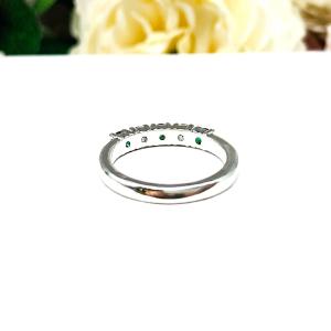 Sterling silver five-stone wedding band with three 3mm round lab-created emeralds and two 3mm round DEF moissanites, shown against a soft floral background.