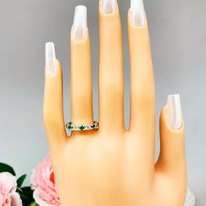 Mannequin hand with long white shimmery nails, displayed against a soft white-gray background with pink and white floral accents. The hand is wearing a sterling silver  five-stone wedding band with three 3mm round lab-created emeralds and two 3mm round DEF moissanites.