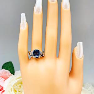 Mannequin hand with long white shimmery nails, displayed against a soft white-gray background with pink and white floral accents. The hand is wearing a sterling silver curved 5-stone band featuring alternating round lab blue sapphires and moissanites. The band has a classic design with the gemstones set in a row with three sapphires and two moissanites. It is featured here with a cushion-cut lab blue sapphire and cz ring (not included).