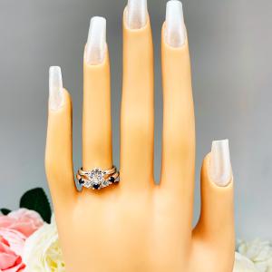 Mannequin hand with long white shimmery nails, displayed against a soft white-gray background with pink and white floral accents. The hand is wearing a sterling silver 5-stone band featuring alternating round lab blue sapphires and moissanites. The band has a classic design with the gemstones set in a row with three sapphires and two moissanites. It is featured here with a round-cut moissanite solitaire ring (not included).