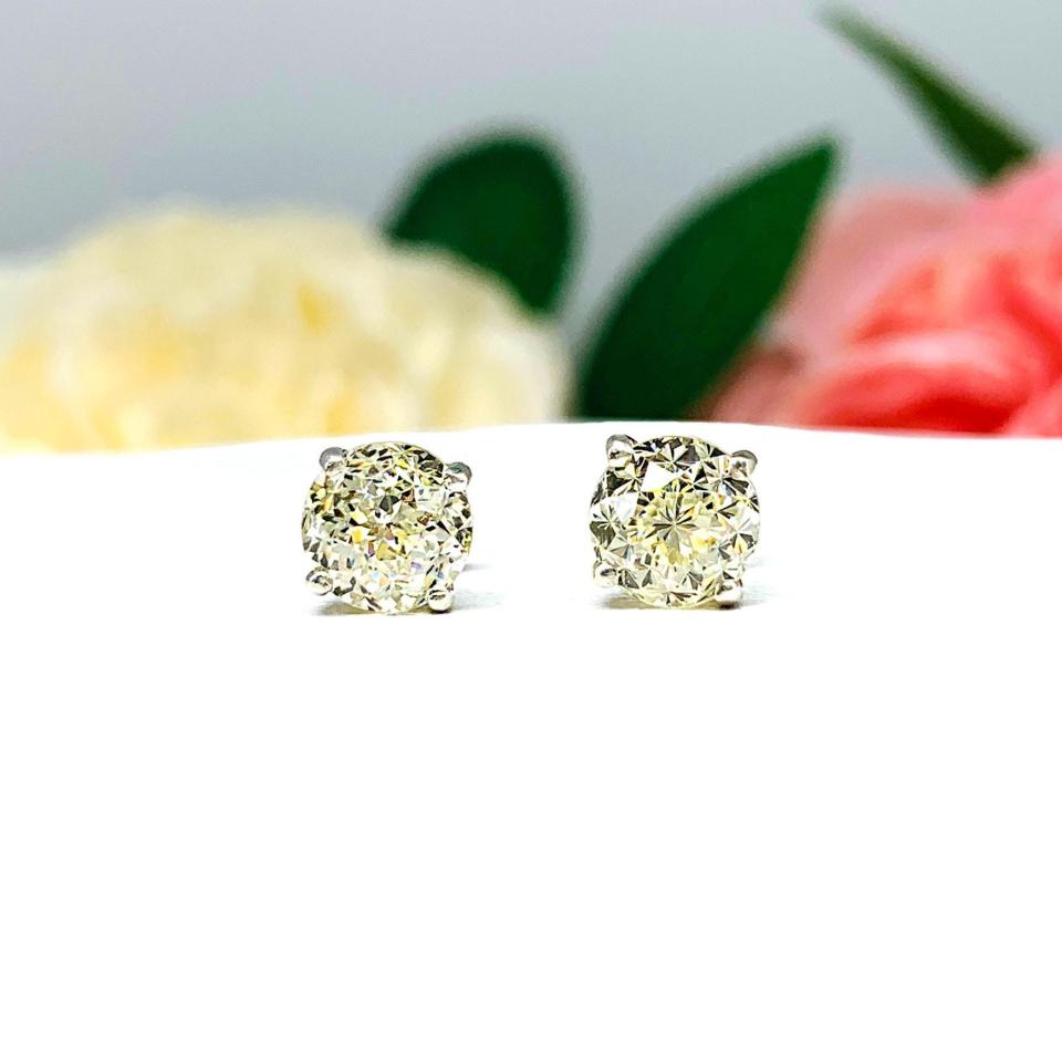 A pair of silver four prong basket stud earrings with light yellow modified Portuguese cut cubic zirconias. The earrings are on a white background with both earrings facing forward to showcase the dazzling brilliance of the Portuguese style faceting.