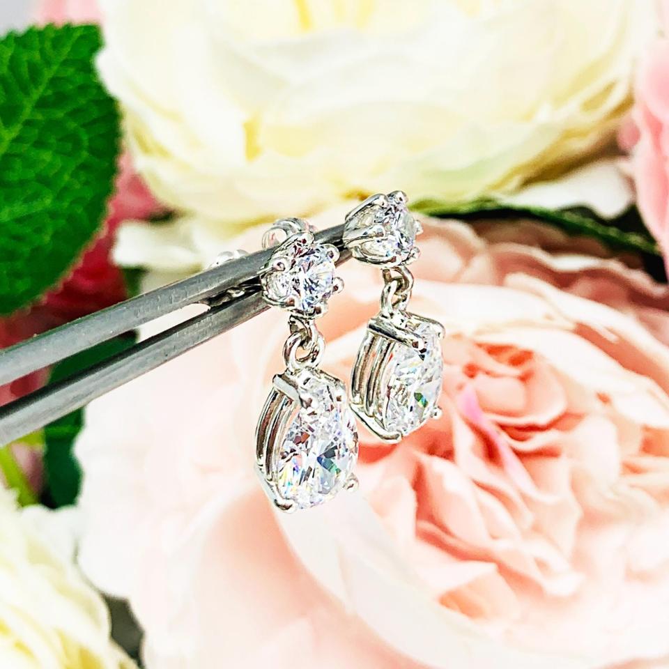 A pair of silver dangle earrings with pear-shaped clear cubic zirconia stones. The top 6-prong stud earrings have a smaller round cubic zirconia stone at the top of the drop.