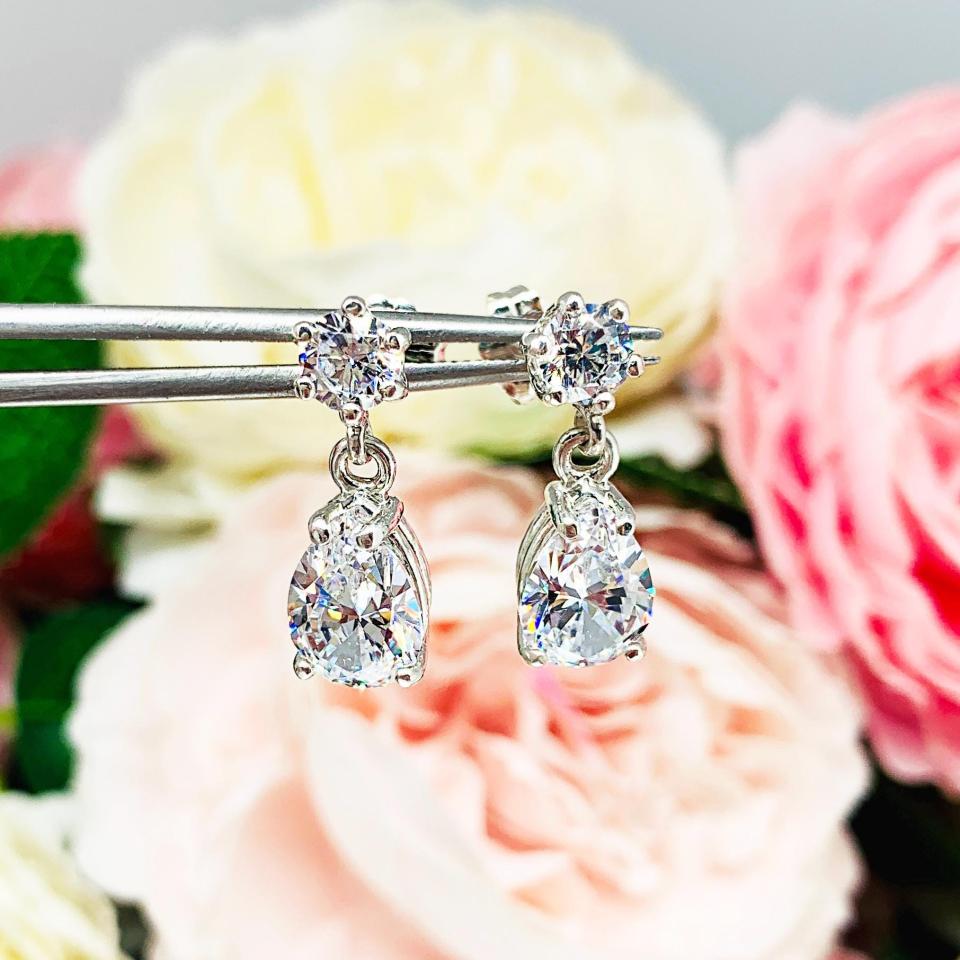 A pair of silver dangle earrings with pear-shaped clear cubic zirconia stones. The top 6-prong stud earrings have a smaller round cubic zirconia stone at the top of the drop.