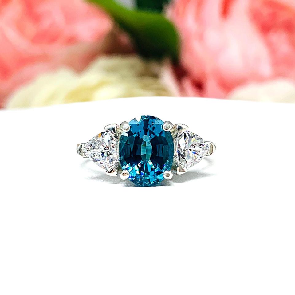 A vivid teal blue oval nanogem glows at the center of this elegant three-stone ring, flanked by sparkling trillion-cut cubic zirconia accents. Set in polished sterling silver, the 9x7mm center stone radiates depth and brilliance, evoking ocean tides and timeless devotion. A graceful blend of color and clarity, perfect for marking a meaningful moment or celebrating personal style.