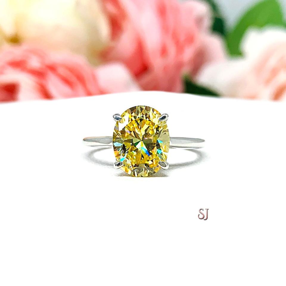 A sterling silver claw prong solitaire cathedral engagement ring featuring a well-faceted, canary yellow 10x8mm cz. Shown on a white surface with a pastel floral background.