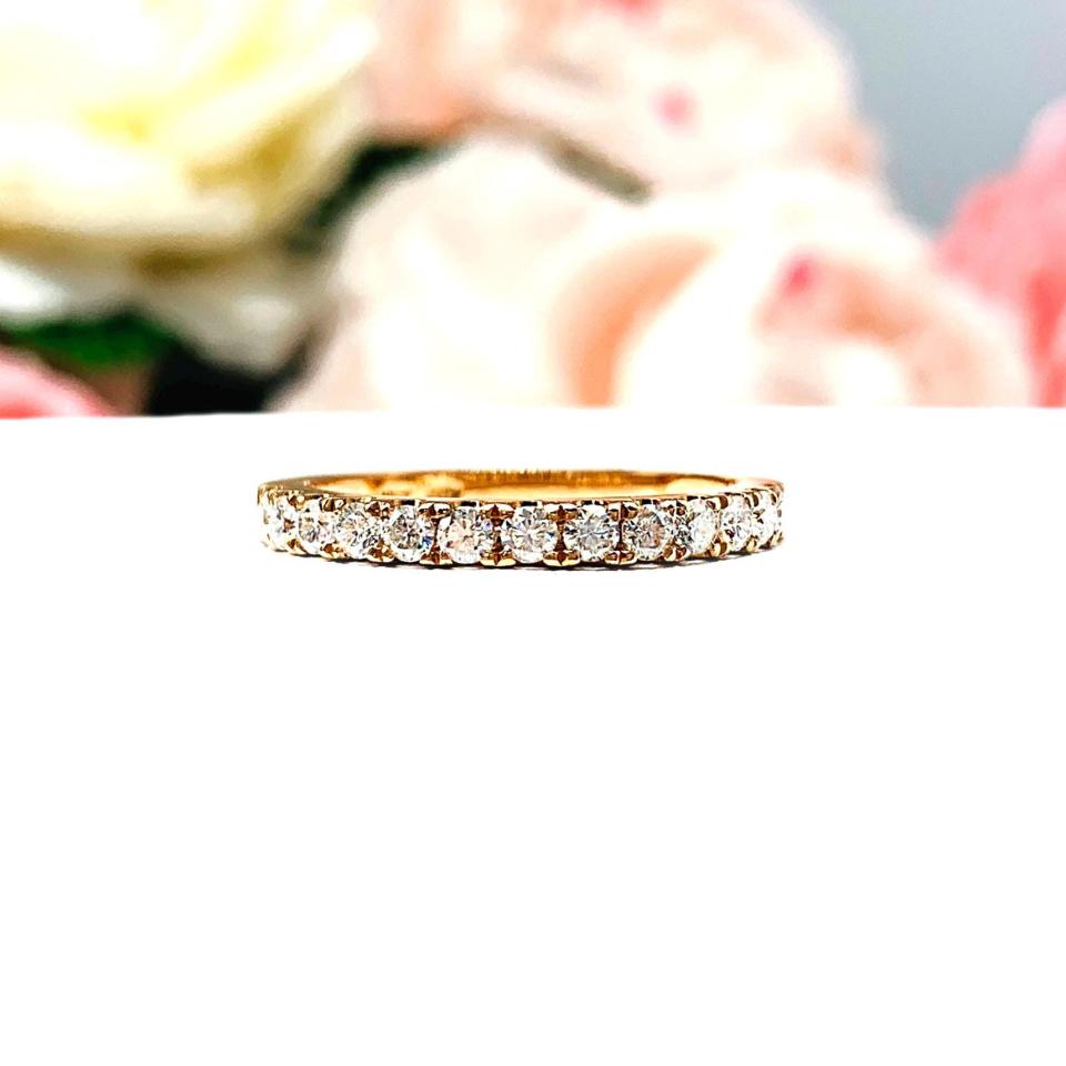 A 10k rose gold 2mm round moissanite wedding band resting on a white surface with pink and white flowers in the background.