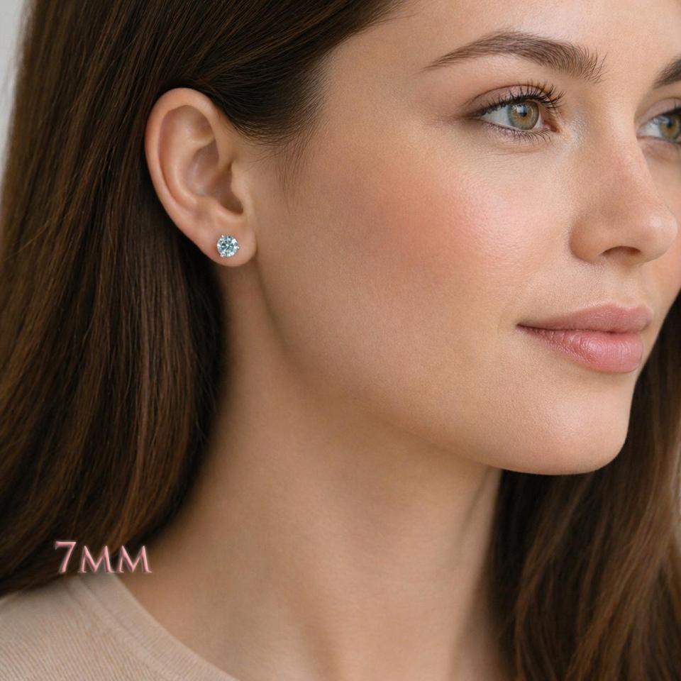 Woman wearing 7mm round blue moissanite martini stud earrings. Model image for size and styling reference — not a photo of the actual earrings.