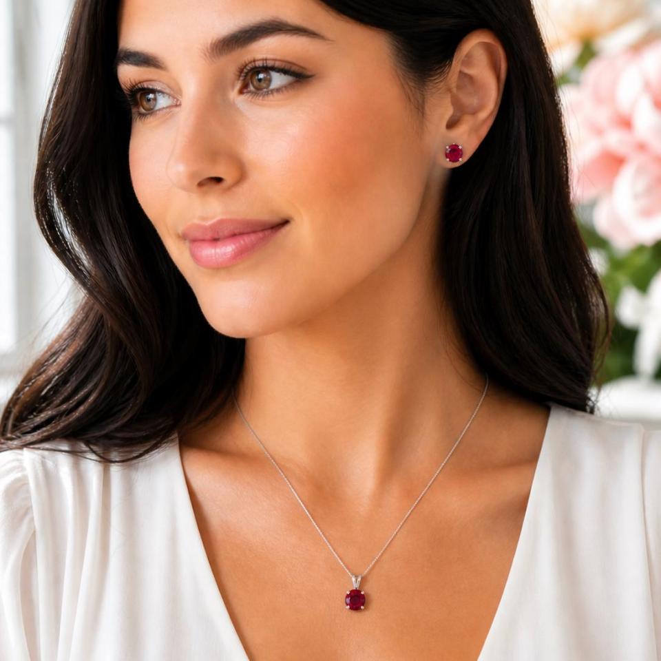 A woman wearing matching round lab ruby earrings and pendant necklace. 'NECKLACE SOLD SEPARATELY' appears in pink text in the image. Model image for size and styling reference — not a photo of the actual necklace.