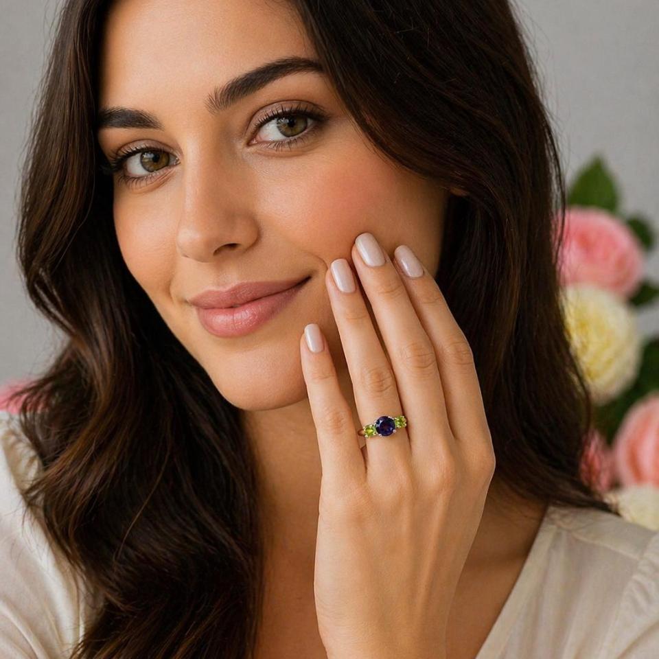 A woman wearing a three-stone sterling silver ring featuring a natural 8mm round African amethyst flanked by two 5mm round Arizona peridot gemstones.
