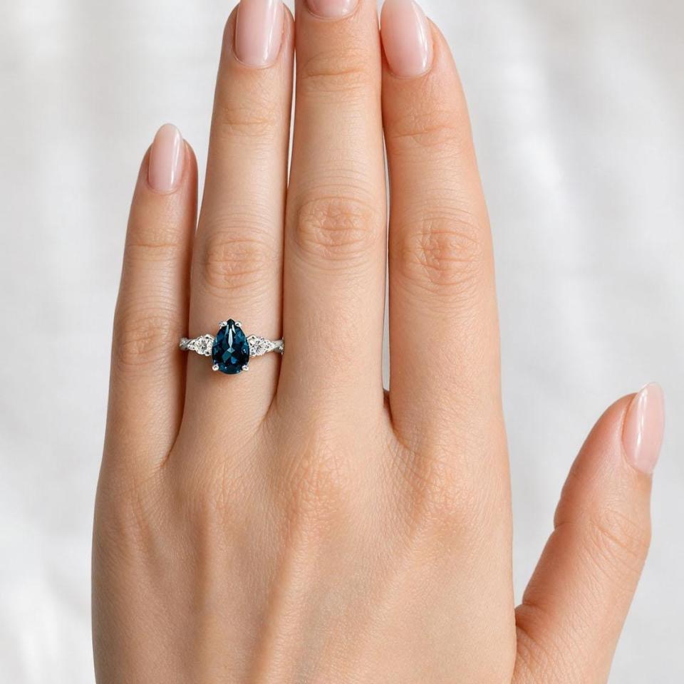 Sterling silver ring, featuring a 10x7mm pear-cut London blue topaz flanked by two round moissanites, shown worn on the hand of a woman. Model image for size and styling reference — not a photo of the actual ring