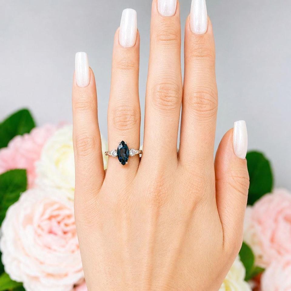 Sterling silver ring, featuring a 14x7mm marquise-cut London blue topaz flanked by two round moissanites, shown worn on the hand of a woman. Model image for size and styling reference — not a photo of the actual ring.