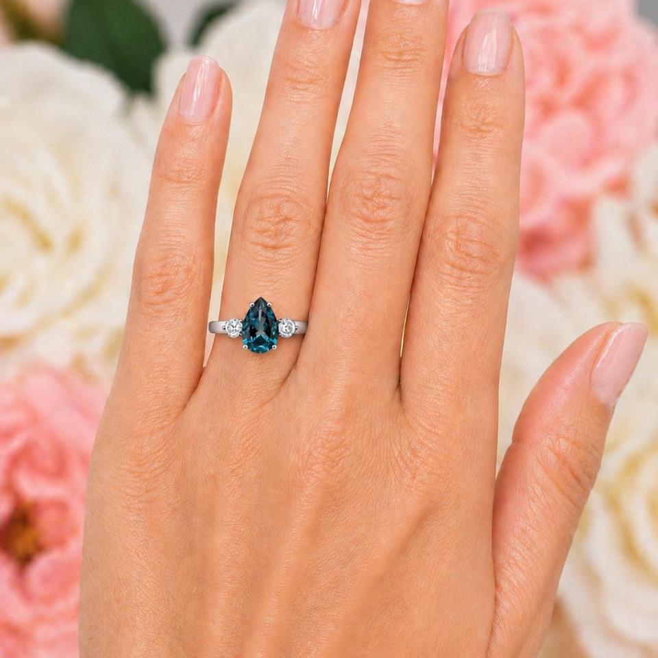 Sterling silver ring, featuring a 10x7mm London blue topaz flanked by two round moissanites, shown worn on the hand of a woman. Model image for size and styling reference — not a photo of the actual ring.