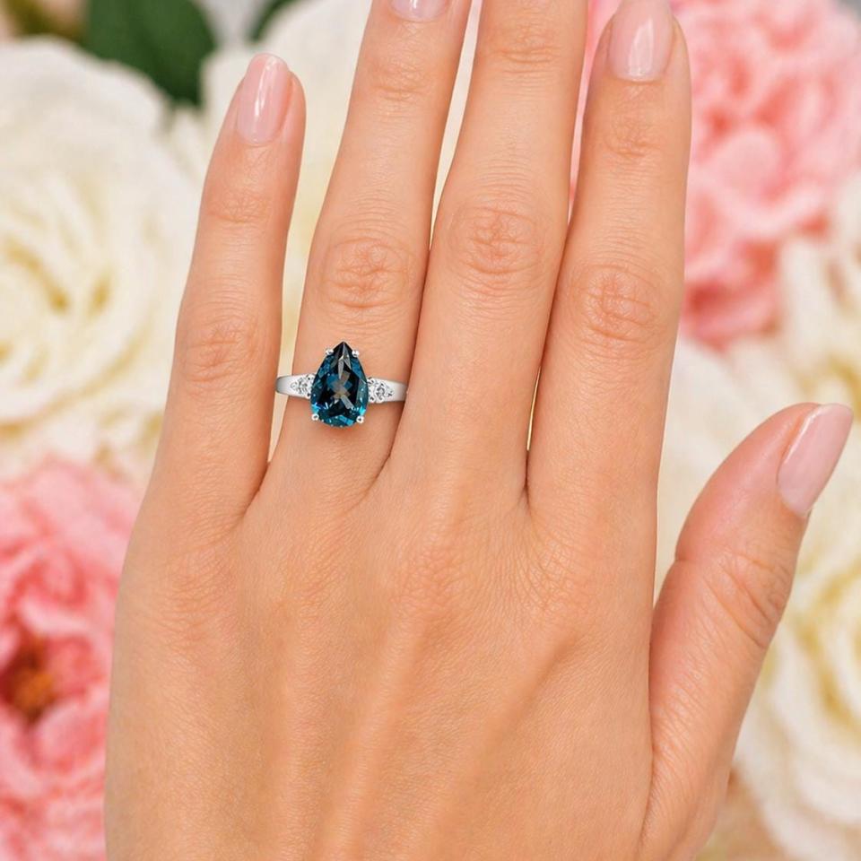Sterling silver ring, featuring a 12x8mm London blue topaz flanked by two round moissanites, shown worn on the hand of a woman. Model image for size and styling reference — not a photo of the actual ring.
