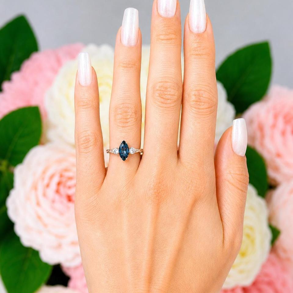 Sterling silver ring, featuring a 10x5mm marquise-cut London blue topaz flanked by two round moissanites, shown worn on the hand of a woman. Model image for size and styling reference — not a photo of the actual ring.