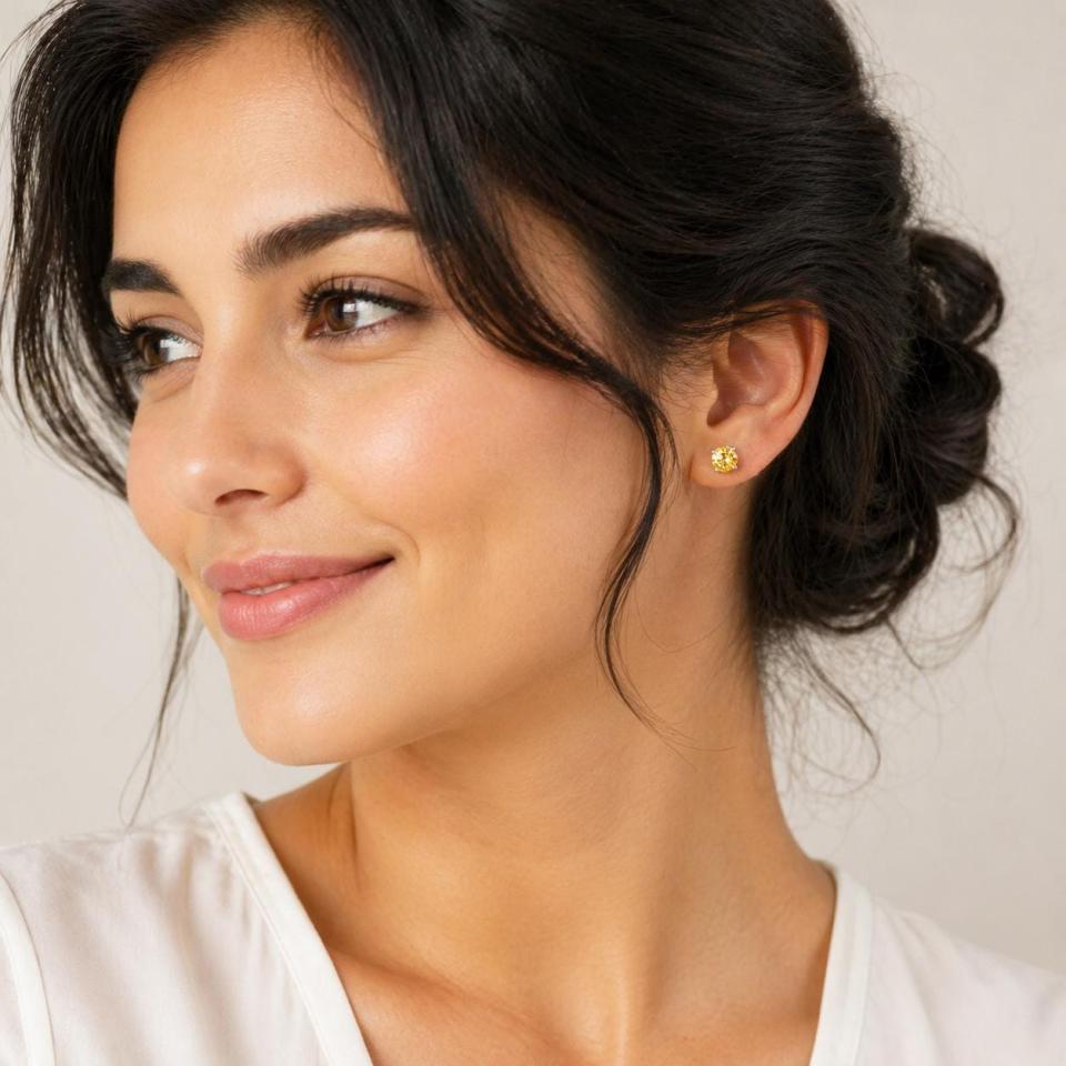A woman wearing silver stud earrings set with 6mm round natural golden citrine gemstones. Model image for size and styling reference — not a photo of the actual earrings.
