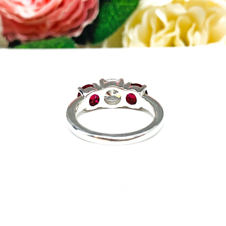 A sterling silver 3-stone ring with a 6mm round brilliant cut cubic zirconia center that radiates icy sparkle, flanked by two 5mm round deep red lab-created rubies.