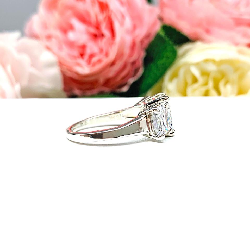 Sterling silver 3-stone engagement ring featuring a 9x7mm radiant cut cubic zirconia center stone with two 7x5mm radiant CZ side stones. The highly polished wide band tapers for comfort. Displayed on a white surface with soft floral background.