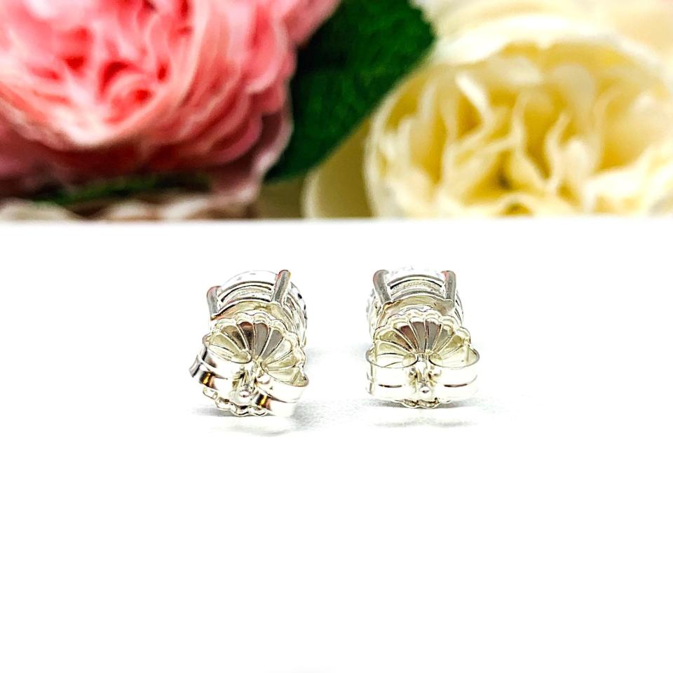 A pair of sterling silver basket stud earrings set with round mixed-brilliant cut lab white sapphires shown on a white surface with pink and white flowers in the background.