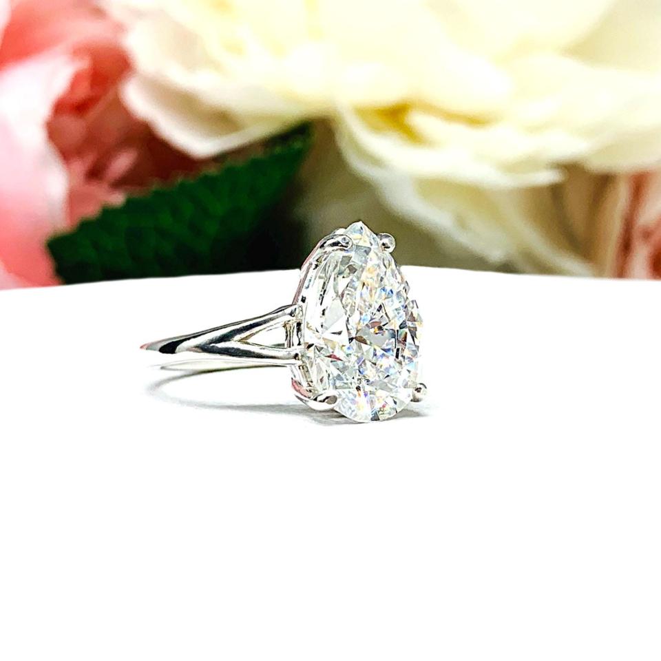 An elegant sterling silver engagement ring featuring a 13x9mm near colorless precision-cut pear cubic zirconia. Displayed on a white surface with a floral background.