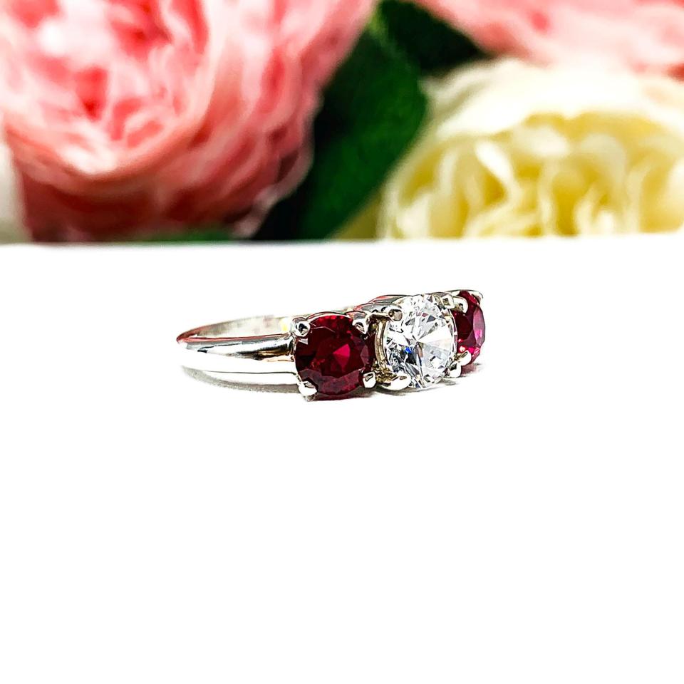 A sterling silver 3-stone ring with a 6mm round brilliant cut cubic zirconia center that radiates icy sparkle, flanked by two 5mm round deep red lab-created rubies.