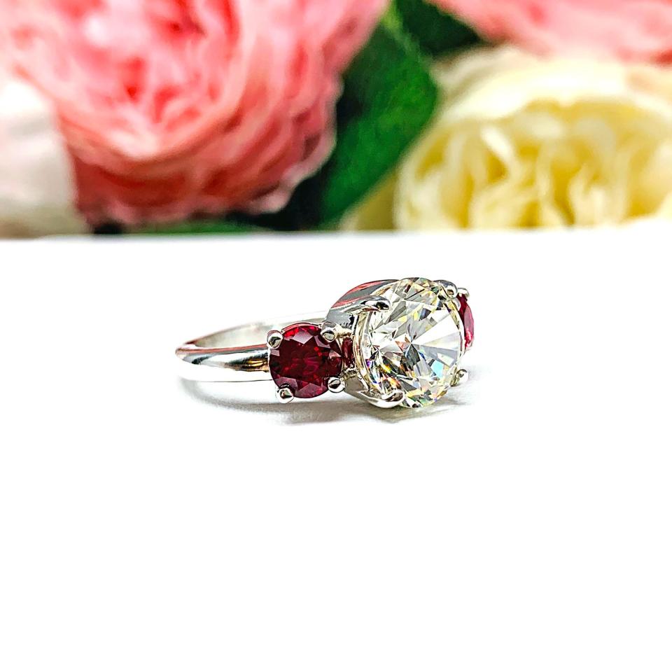 A sterling silver 3-stone ring with a 9mm near colorless round brilliant cut cubic zirconia center that radiates icy sparkle, flanked by two 5mm round deep red lab-created rubies.