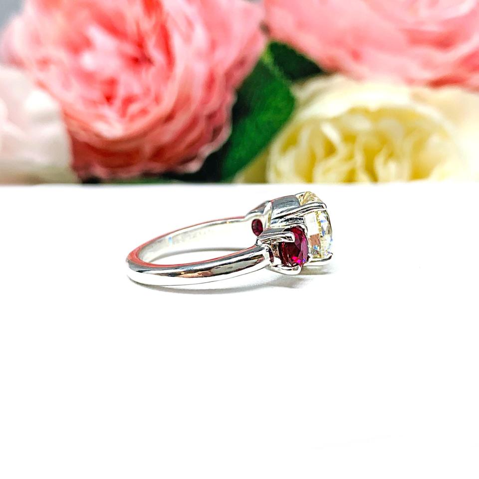A sterling silver 3-stone ring with a 9mm near colorless round brilliant cut cubic zirconia center that radiates icy sparkle, flanked by two 5mm round deep red lab-created rubies.