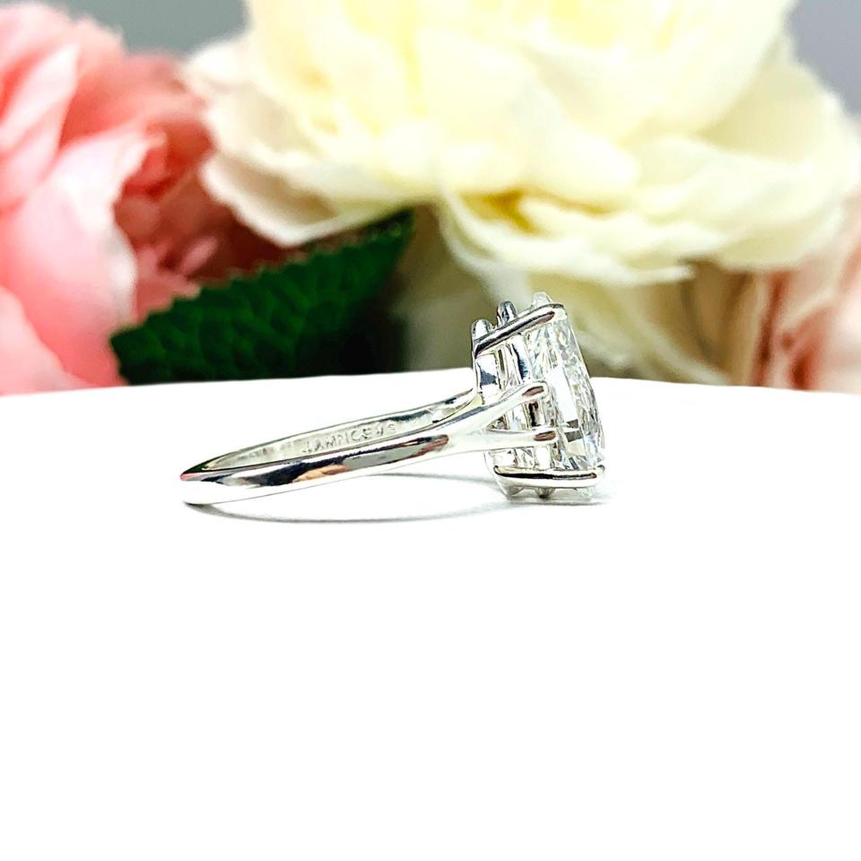 An elegant sterling silver engagement ring featuring a 13x9mm near colorless precision-cut pear cubic zirconia. Displayed on a white surface with a floral background.