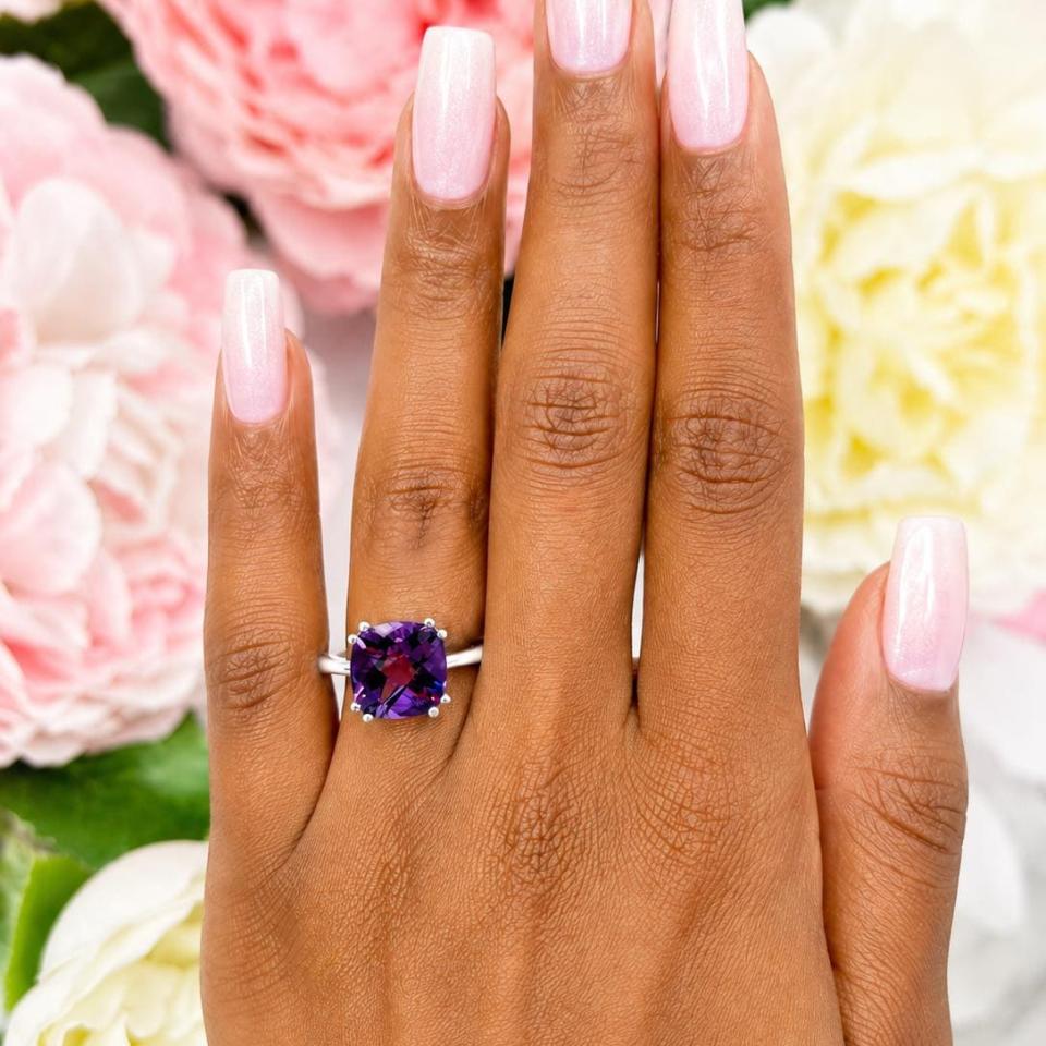 Sterling silver solitaire ring featuring a 10mm checkerboard cushion-cut vibrant African amethyst worn on a woman's hand. Model image for size and styling reference — not a photo of the actual ring