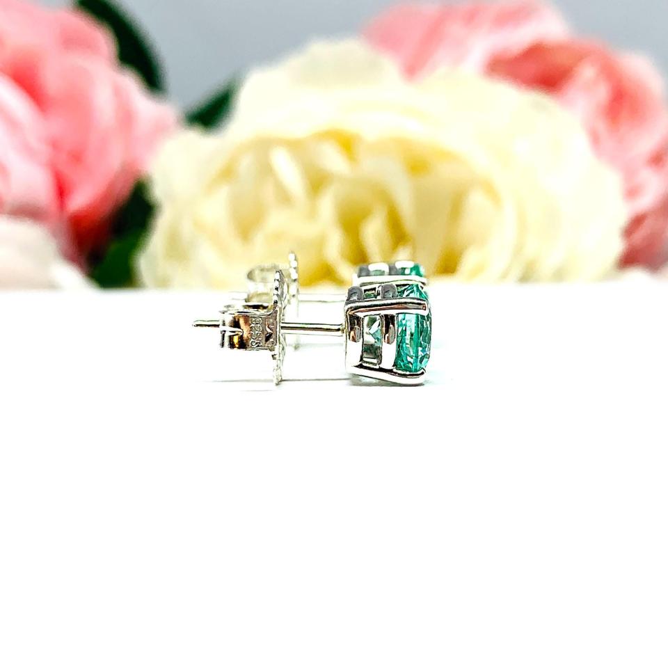 A pair of silver basket earrings set with 7mm round sea foam green lab spinels, displayed with both earrings facing to the right to showcase the centrally located posts and butterfly friction clasps. The earrings are shown on a white background.