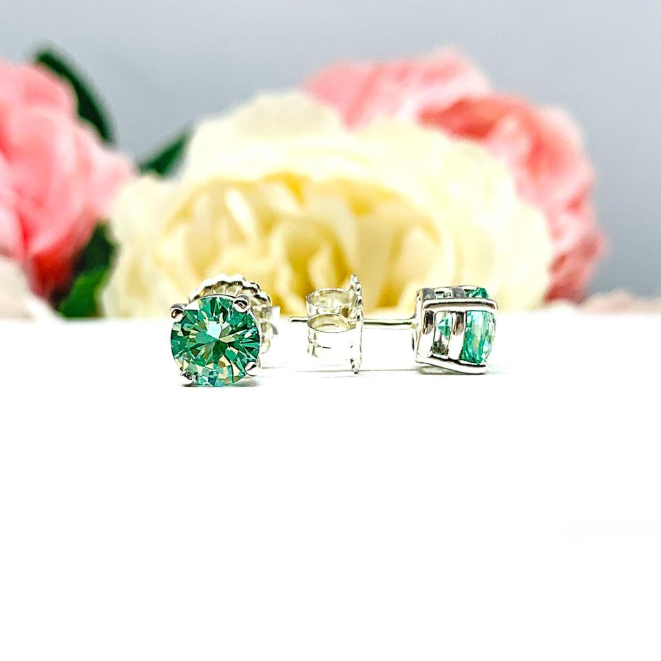 A pair of silver basket earrings set with 7mm round sea foam green lab spinels, displayed with the left earring facing the front to showcase the brilliant cutting of the stones and the right earring facing to the right to show the center post and butterfly friction clasp. The earrings are shown on a white background.