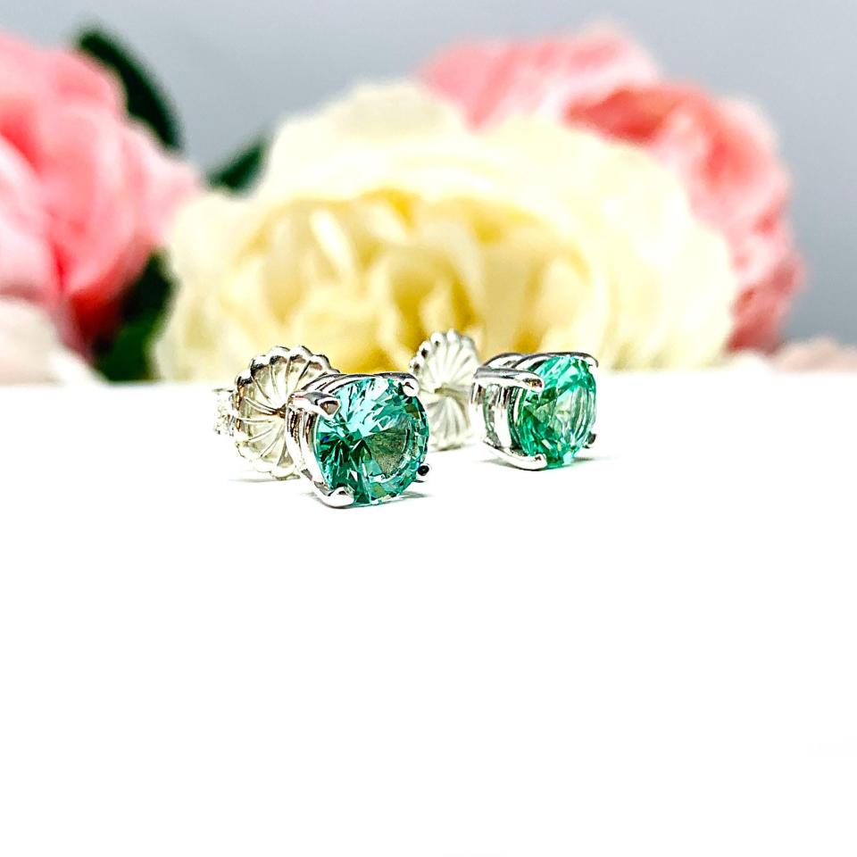 A pair of silver basket earrings set with 7mm round sea foam green lab spinels, displayed with both earrings facing slightly to the right to showcase the centrally located posts and butterfly friction clasps. The earrings are shown on a white background.