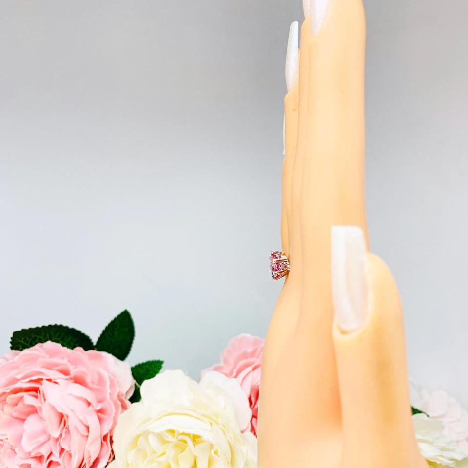 Mannequin hand with long white shimmery nails, displayed against a soft white-gray background with pink and white floral accents. The hand is wearing a sterling silver ring with an 8x6mm oval lab created padparadscha sapphire set in a 6-prong setting.