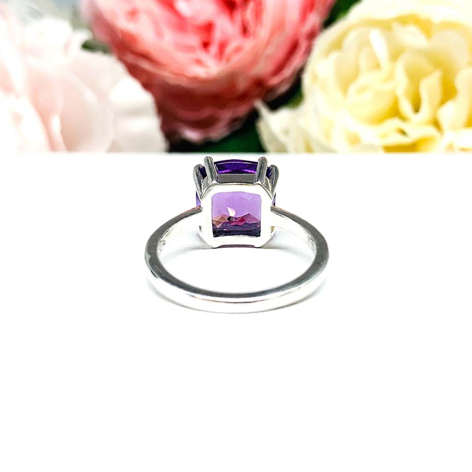Sterling silver solitaire ring featuring a 10mm checkerboard cushion-cut vibrant African amethyst gemstone. The vibrant purple gem ring is set against a soft floral background that enhances the ring’s natural elegance.