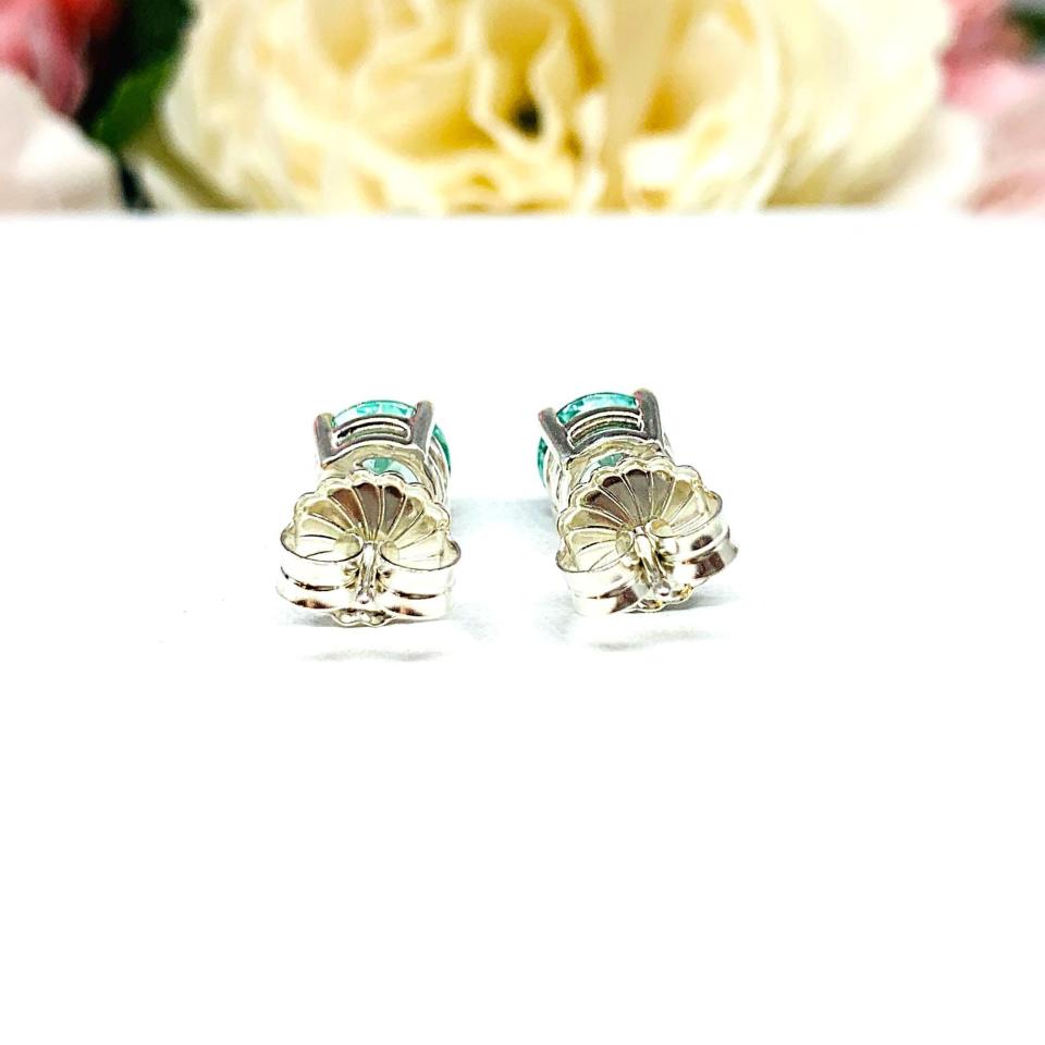A pair of silver basket earrings set with 7mm round sea foam green lab spinels, displayed with both earrings facing to towards the back to showcase the centrally located posts and butterfly friction clasps. The earrings are shown on a white background.