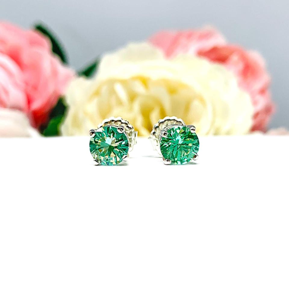 A pair of silver basket earrings set with 7mm round sea foam green lab spinels, displayed with both earrings facing the front to showcase the brilliant cutting of the stones and that the settings have four prongs. The earrings are shown on a white background.