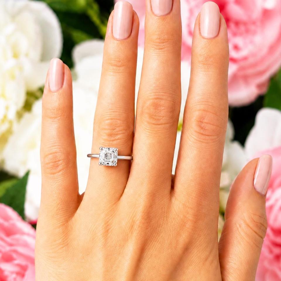 A woman's hand wearing a sterling silver 4-prong 7mm asscher cut DEF moissanite solitaire engagement ring. Model image for size and styling reference — not a photo of the actual ring.