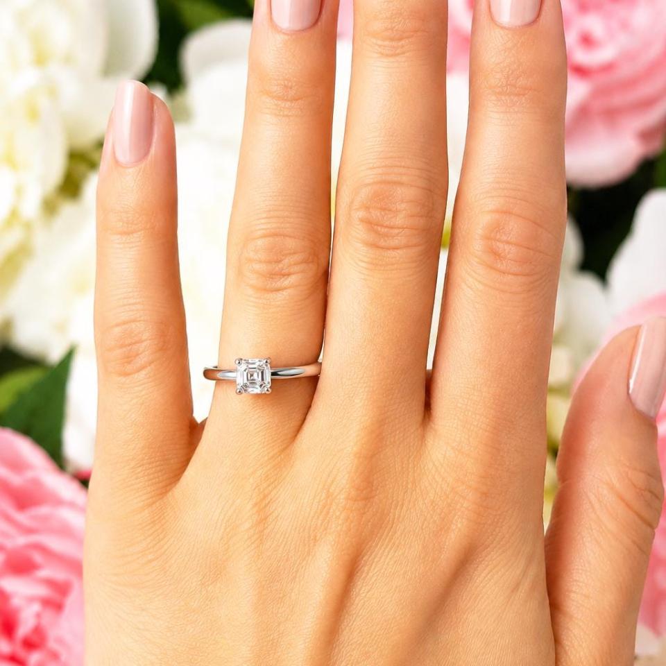 A woman's hand wearing a sterling silver 4-prong 5mm asscher cut DEF moissanite solitaire engagement ring. Model image for size and styling reference — not a photo of the actual ring.