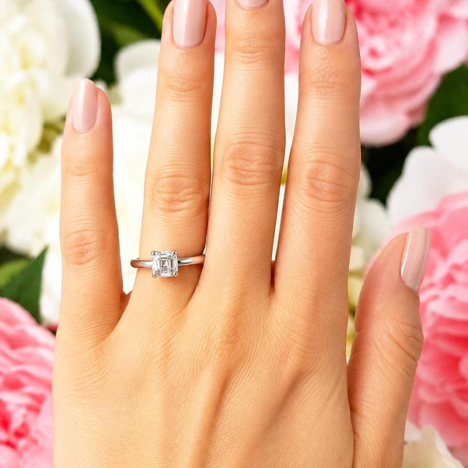 A woman's hand wearing a sterling silver 4-prong 6mm asscher cut DEF moissanite solitaire engagement ring. Model image for size and styling reference — not a photo of the actual ring.