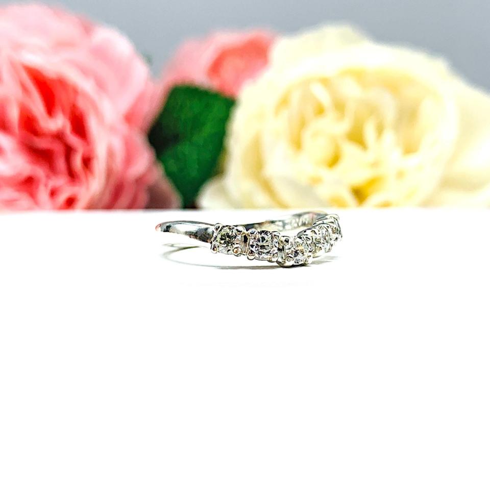 Sterling silver 5-stone curved wedding band featuring 3mm round precision faceted near colorless cubic zirconia stones in prong settings, displayed against a soft floral background.